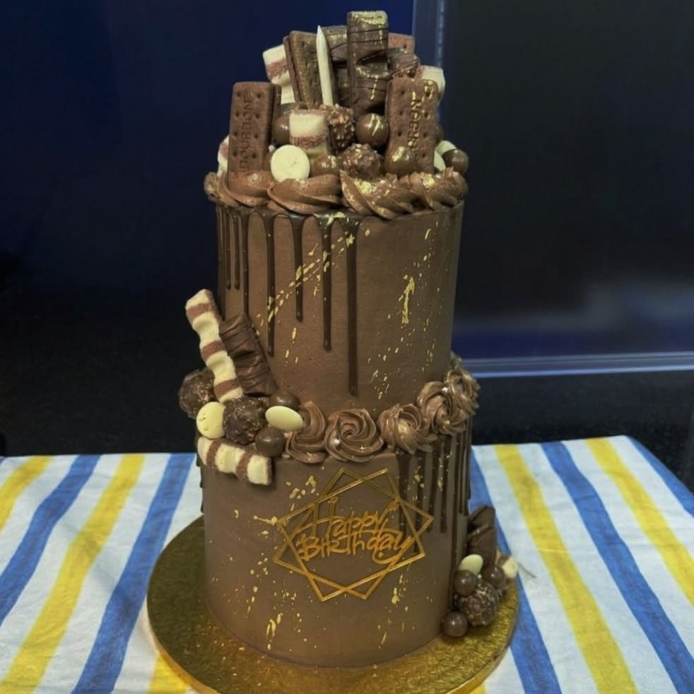 A tall chocolate drip cake with chocolate spheres and a gold topper