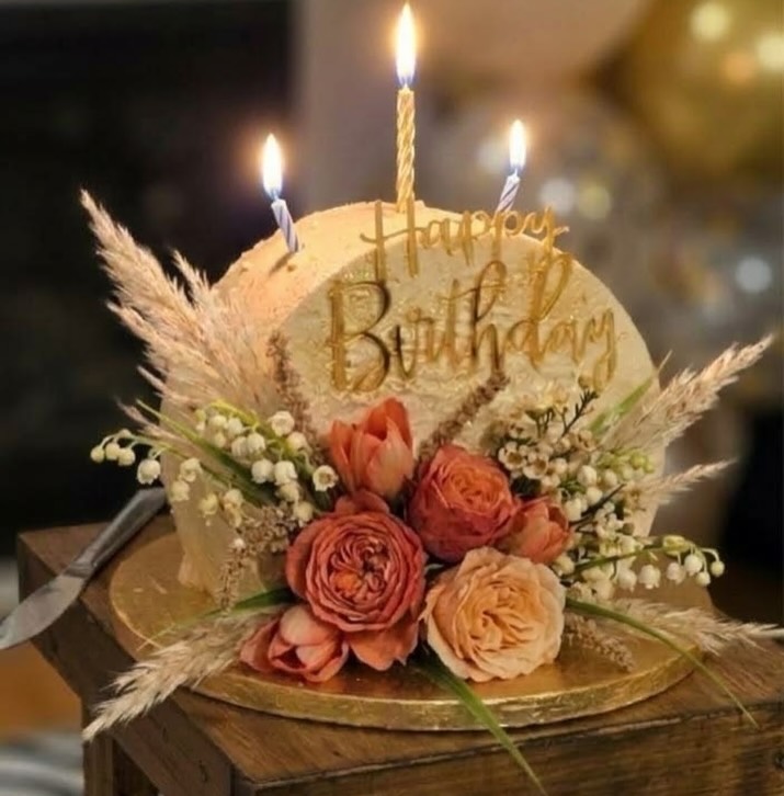 A boho-style birthday cake with fresh roses, pampas grass and lit candles by Sugar Delight