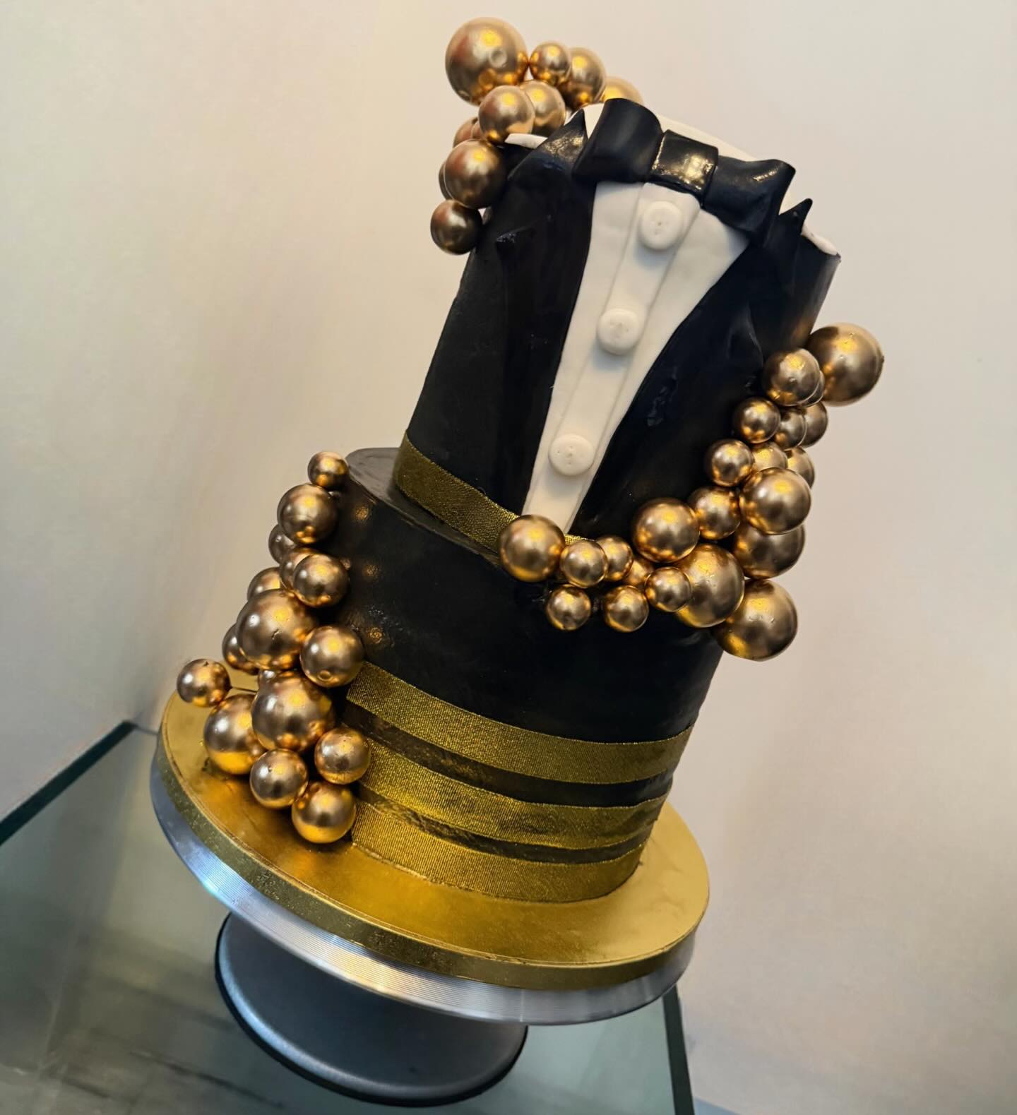 A two-tier black and gold tuxedo cake with a bow tie and gold spheres
